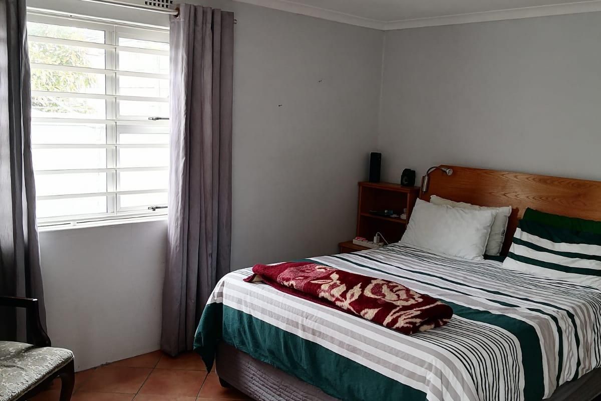 A bedroom featuring terracotta floor tiles, security bars on the window, and modern track lighting, offering a functional and well-lit living space.