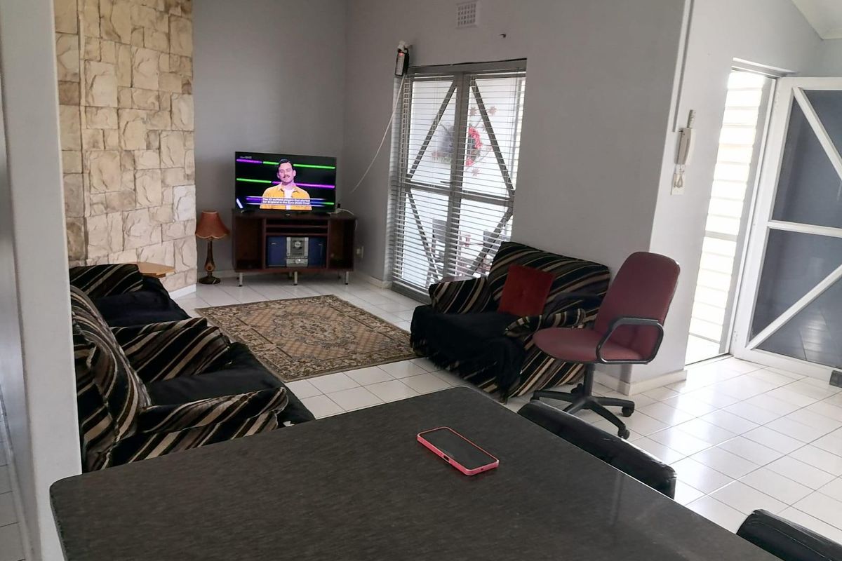 A living room featuring a stone accent wall, tiled flooring, and natural light through aluminium-framed windows and a security gate.
