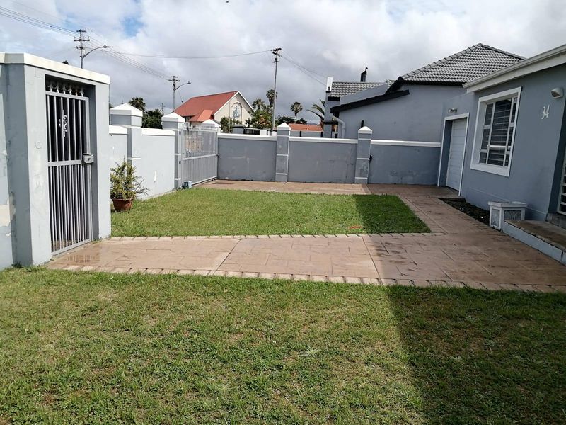 Front exterior view of the property featuring a paved walkway, lawn area, perimeter wall, and secure metal gates.