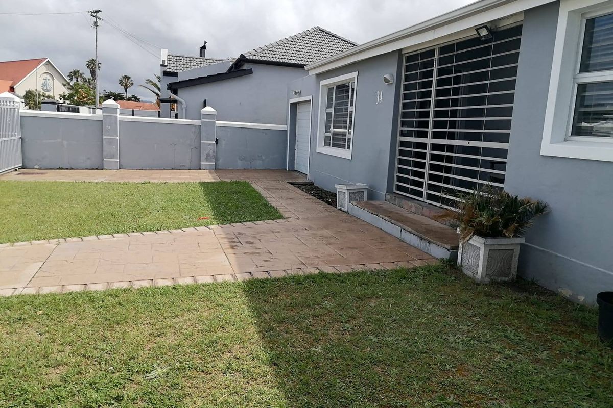 Rear exterior view of the property featuring a paved walkway, lawn area, and secure access points with security bars.