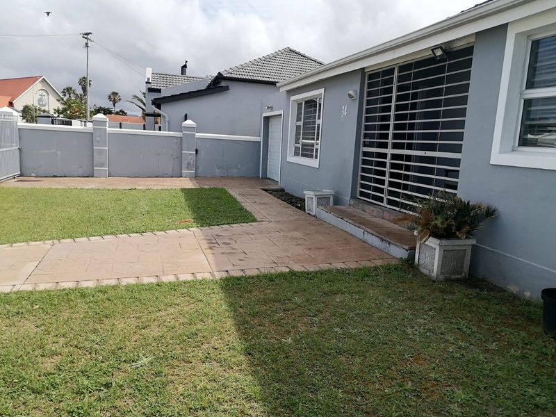 Rear exterior view of the property featuring a paved walkway, lawn area, and secure access points with security bars.