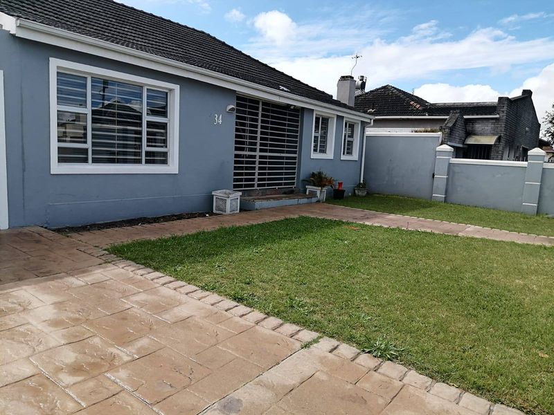 Front exterior view of a single-story house featuring a paved driveway, front lawn, security gate, and boundary wall.