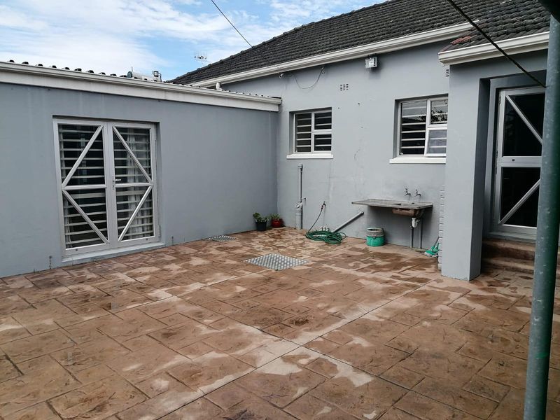 A paved rear courtyard area featuring an external utility sink, security gates, and direct access to the main dwelling.