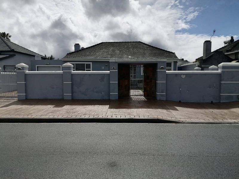 Front elevation of a single-story house featuring a perimeter wall, gated entrance, and tiled roof, showing signs of exterior wear.
