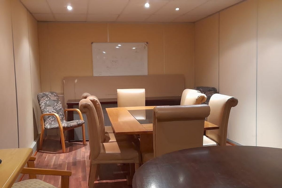 A functional office meeting room featuring modular wall paneling, recessed ceiling lighting, and a wood-look laminate floor.