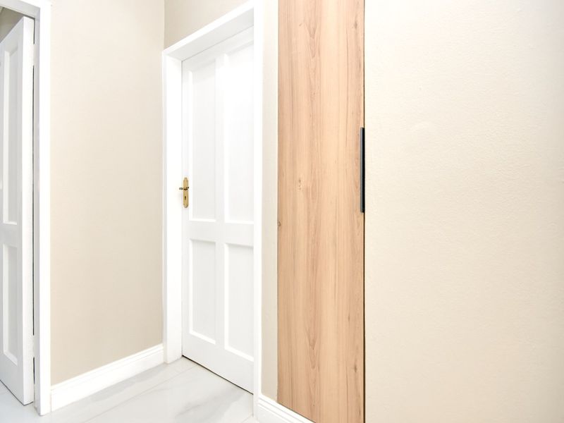 A clean, neutral hallway featuring white internal doors and integrated wood-finish cabinetry with modern hardware.