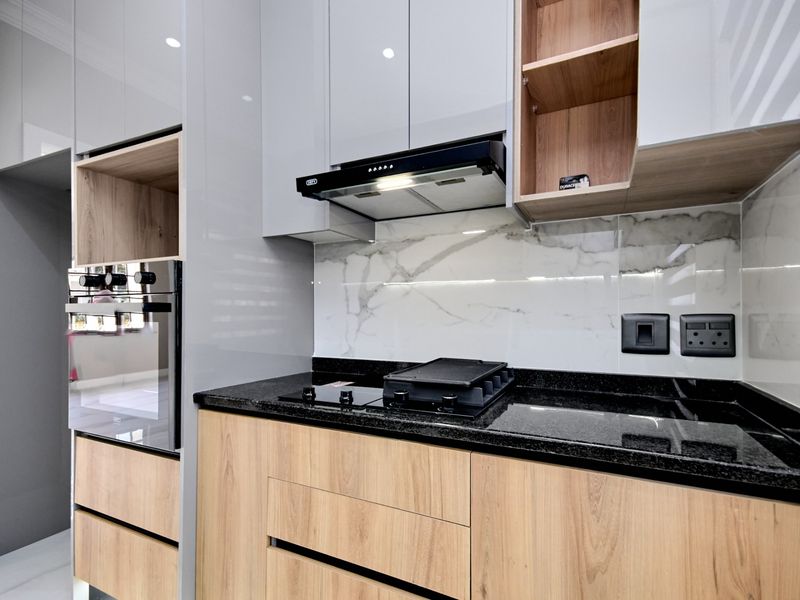 Modern kitchen featuring high-gloss cabinetry, wood-grain accents, granite countertops, a marble-look splashback, and integrated built-in appliances.