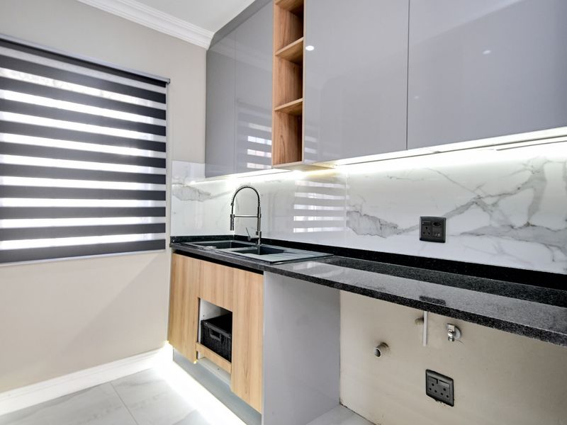 Modern kitchen area featuring sleek glossy cabinetry, marble-look splashback, granite countertops, and integrated under-cabinet lighting.