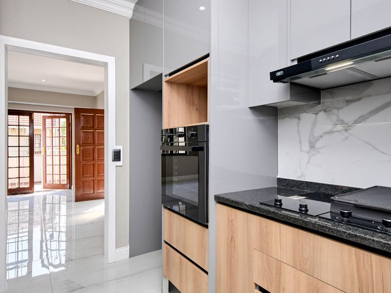 Modern kitchen featuring high-gloss cabinetry, built-in oven, extractor fan, and stone countertops, leading through to a bright hallway with wooden doors.