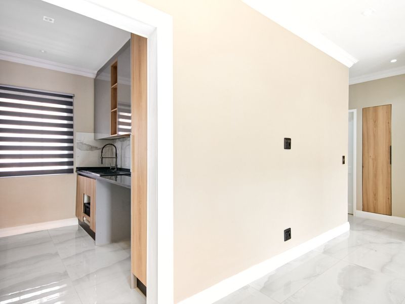 A modern, minimalist kitchen featuring sleek two-tone cabinetry, stone countertops, and high-quality porcelain floor tiles, viewed from an adjacent hallway.