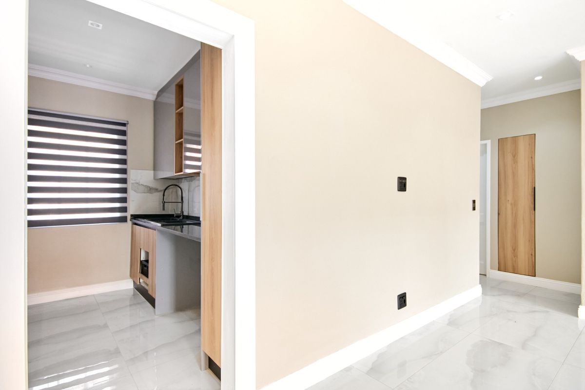 A modern, minimalist kitchen featuring sleek two-tone cabinetry, stone countertops, and high-quality porcelain floor tiles, viewed from an adjacent hallway.