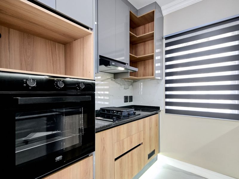 Modern kitchen featuring sleek grey and wood-tone cabinetry, granite countertops, built-in oven, gas hob, and integrated under-cabinet lighting.