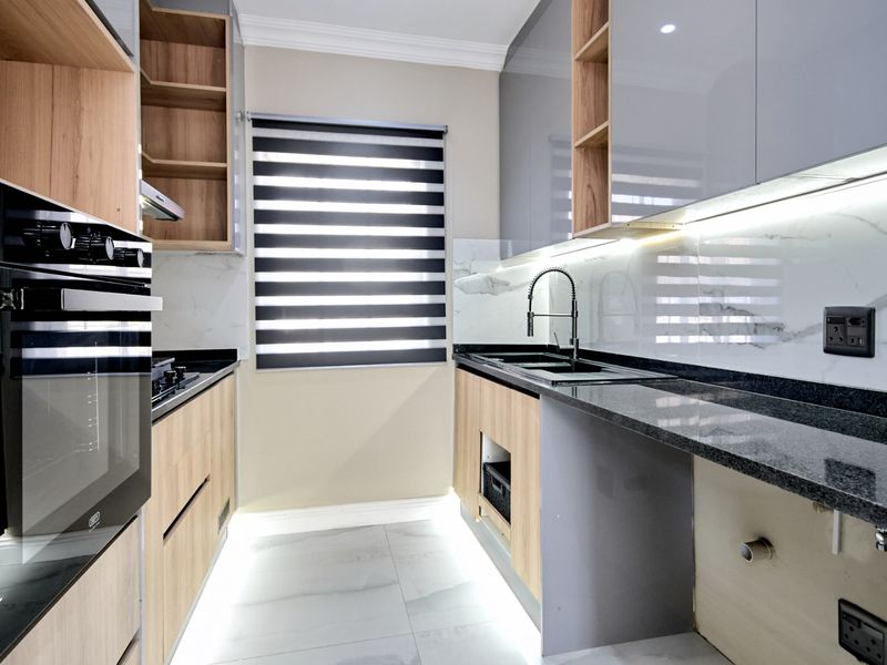 Modern galley kitchen featuring high-gloss grey and wood-grain cabinetry, granite countertops, marble-look splashbacks, and integrated lighting, awaiting final finishing touches.