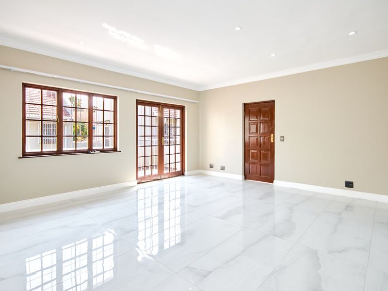 A bright, spacious living area featuring polished marble-look floor tiles, recessed lighting, and classic timber-framed doors and windows.