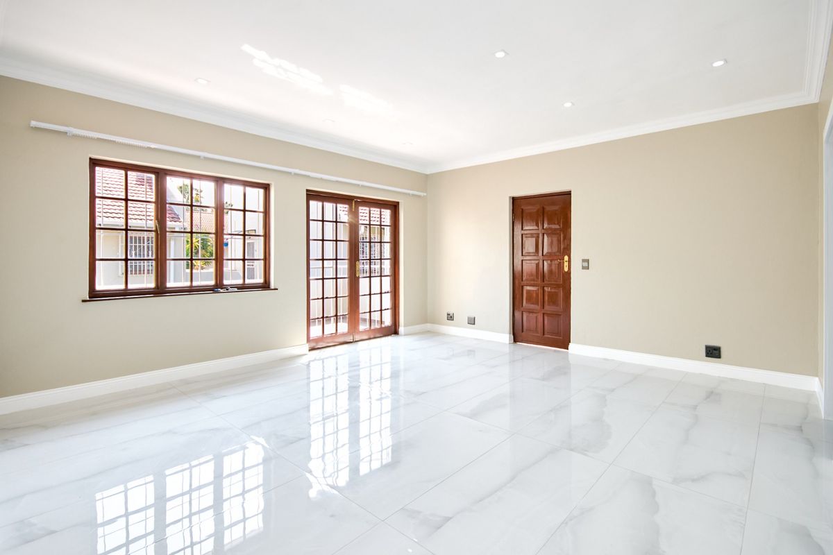 A bright, spacious living area featuring polished marble-look floor tiles, recessed lighting, and classic timber-framed doors and windows.
