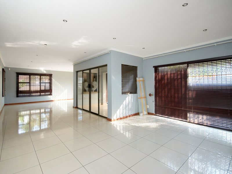 Spacious, light-filled living area featuring neutral tiled flooring, recessed downlights, and large sliding glass doors with fitted venetian blinds.