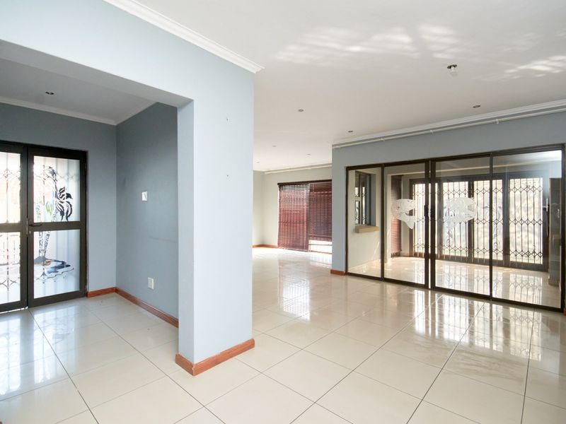 Spacious open-plan living area featuring neutral tiled flooring, recessed lighting, and large sliding glass doors with security gates leading to the exterior.