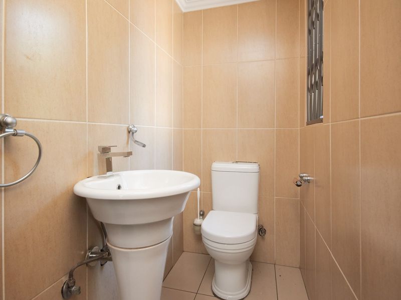 A compact, well-maintained guest bathroom featuring neutral wall tiles, a pedestal basin, and a standard toilet.