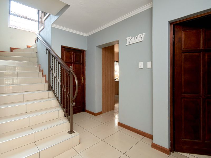 A bright entrance hallway featuring a tiled staircase with a decorative wrought iron balustrade and access to multiple rooms through timber panel doors.
