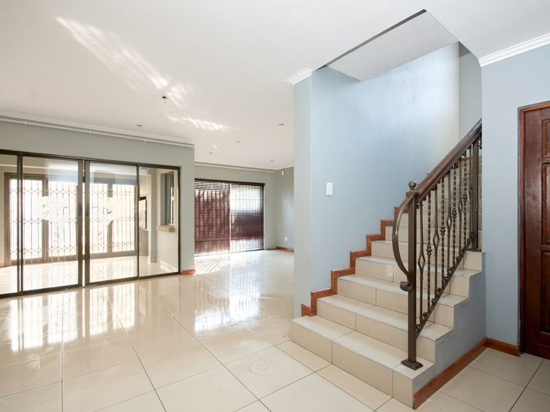 Spacious open-plan living area featuring tiled flooring, a staircase with a decorative wrought iron balustrade, and large sliding glass doors.