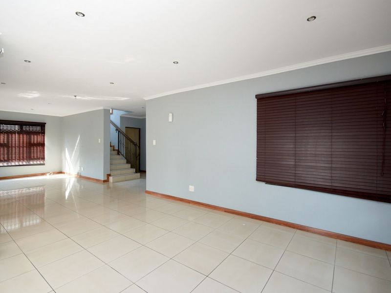 Spacious, light-filled living area featuring neutral tiled flooring, recessed lighting, and a staircase with a metal balustrade.