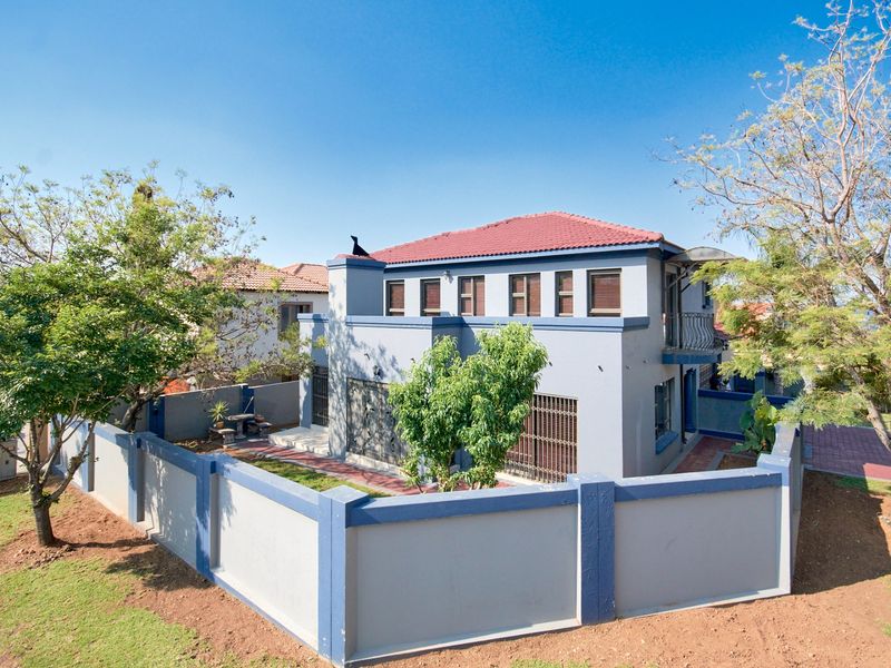A two-story residential property featuring a tiled roof, secure perimeter wall, and a balcony, set within a landscaped garden area.