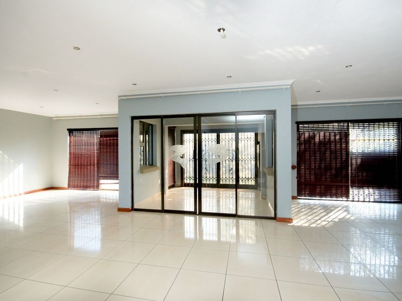 Spacious, open-plan living area featuring polished tile flooring, recessed lighting, and large sliding glass doors with security gates and venetian blinds.