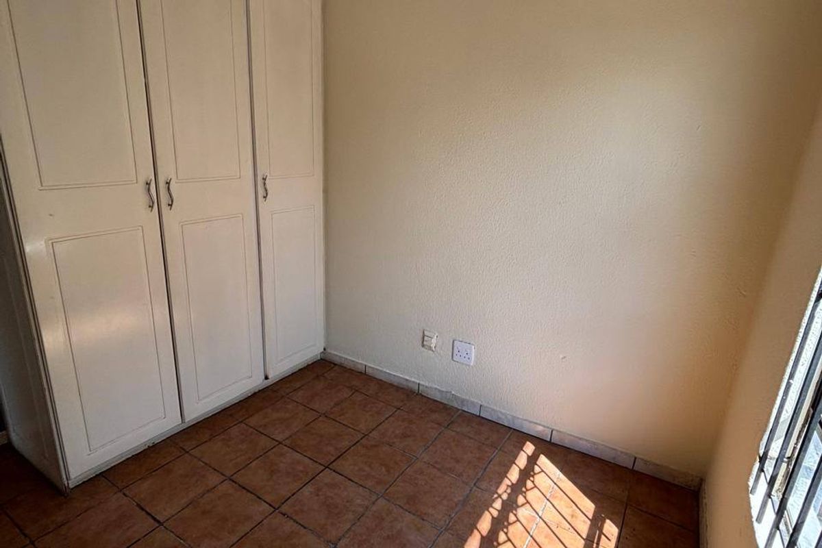 A vacant bedroom featuring built-in cupboards, tiled flooring, and security bars on the window, offering a blank canvas for potential updates.