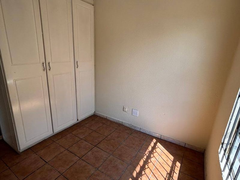 A vacant bedroom featuring built-in cupboards, tiled flooring, and security bars on the window, offering a blank canvas for potential updates.