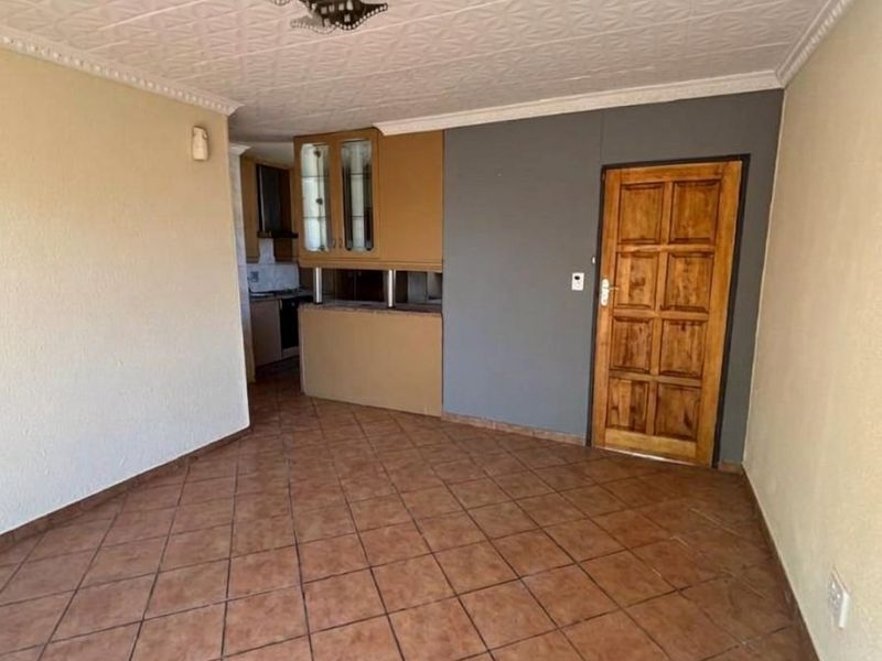 An open-plan living area featuring tiled flooring, textured ceiling tiles, and a compact kitchen area with built-in cabinetry and a breakfast counter.