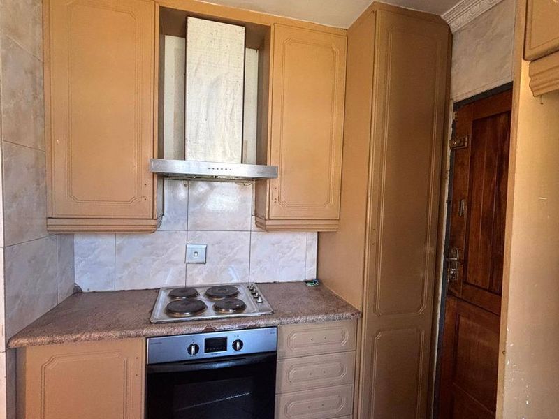 Compact kitchen featuring built-in cabinetry, an integrated oven and hob, tiled backsplash, and tiled flooring, offering a functional layout with potential for modernization.