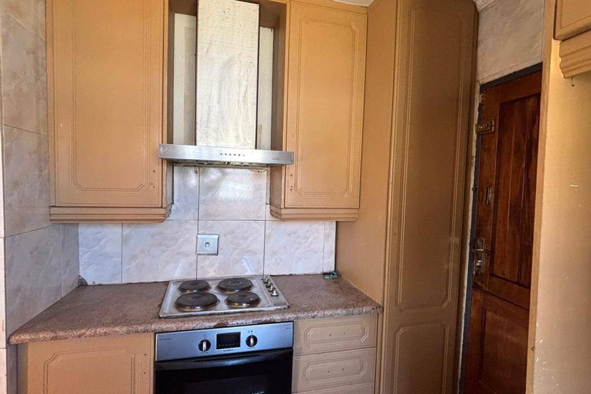 Compact kitchen featuring built-in cabinetry, an integrated oven and hob, tiled backsplash, and tiled flooring, offering a functional layout with potential for modernization.