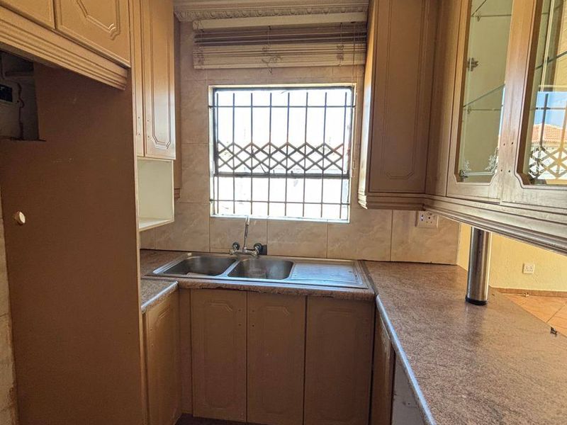 A compact kitchen featuring dated built-in cabinetry, laminate countertops, a double stainless steel sink, and tiled flooring, ready for a modern renovation.