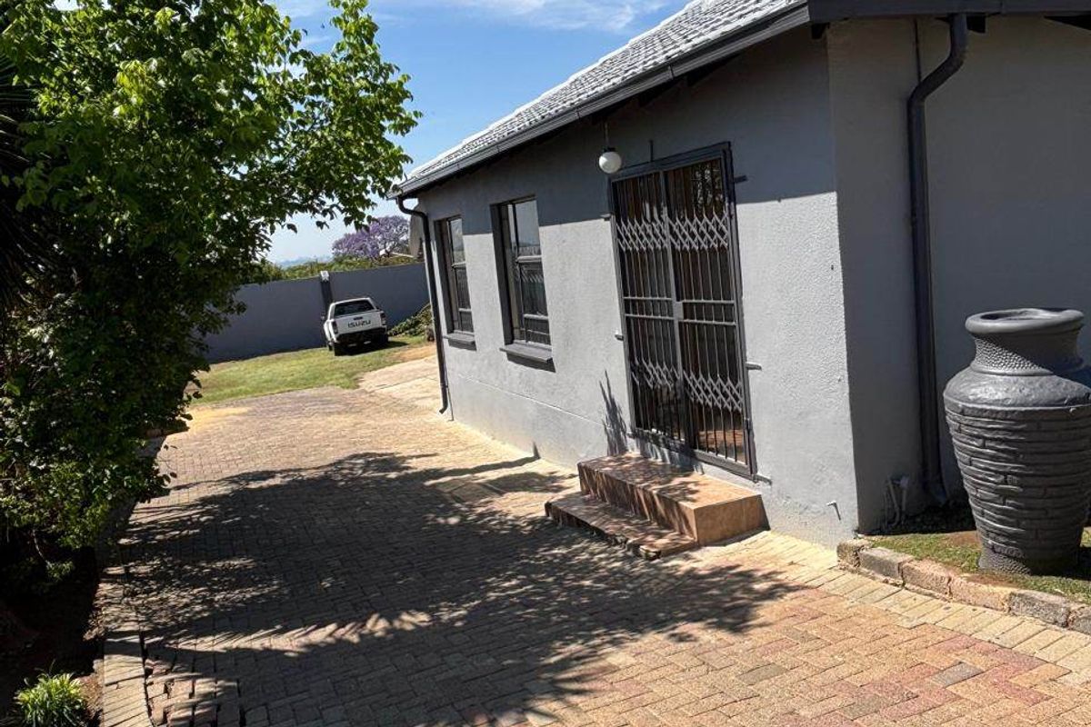 Rear exterior view of the property featuring a paved driveway, security gate, and tiled roof structure.