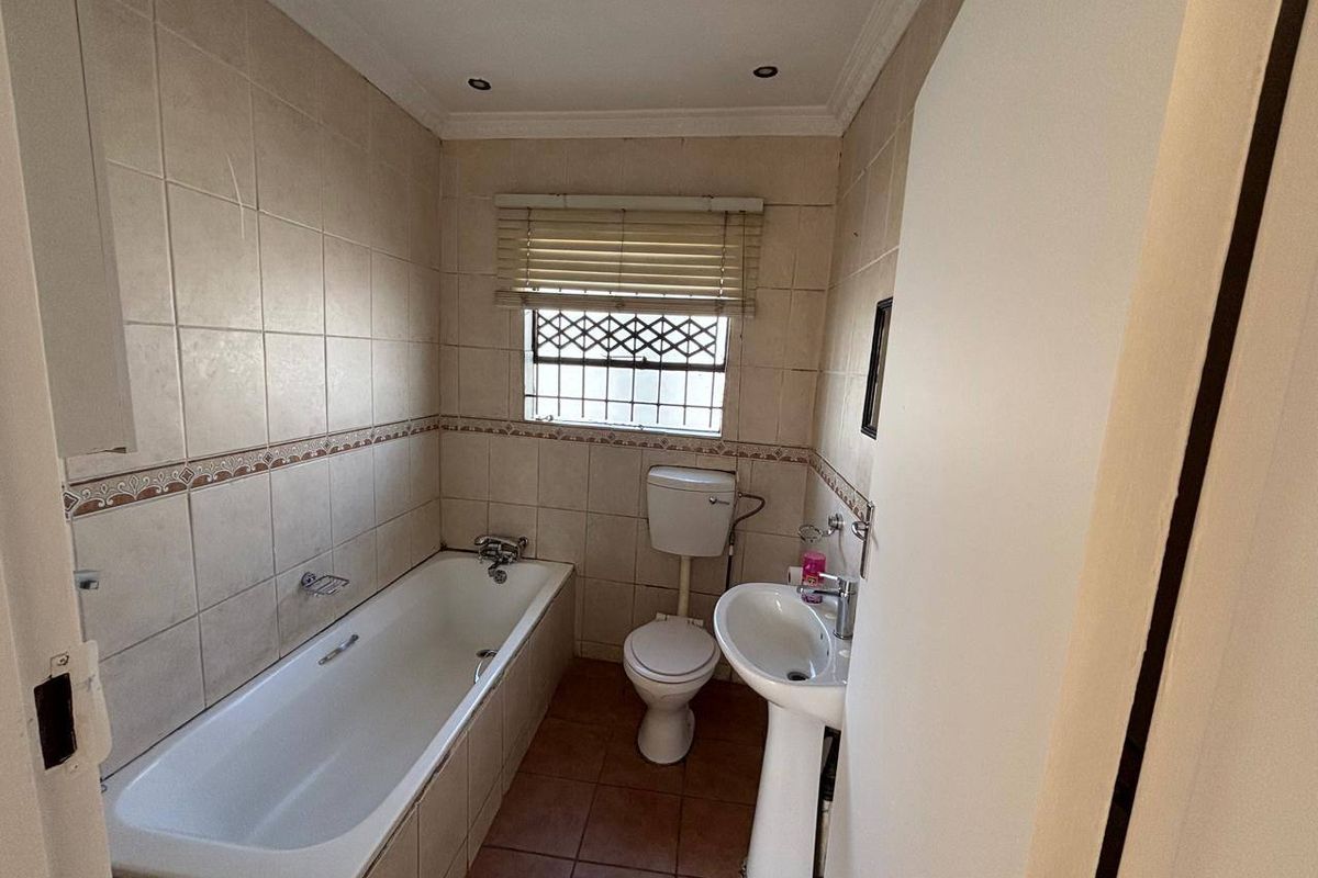 A functional bathroom featuring a bathtub, pedestal basin, and toilet, finished with neutral ceramic wall and floor tiles.