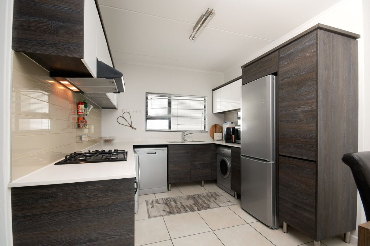 Modern kitchen featuring dark wood-grain cabinetry, white countertops, tiled backsplash, gas hob, extractor fan, and integrated space for appliances.
