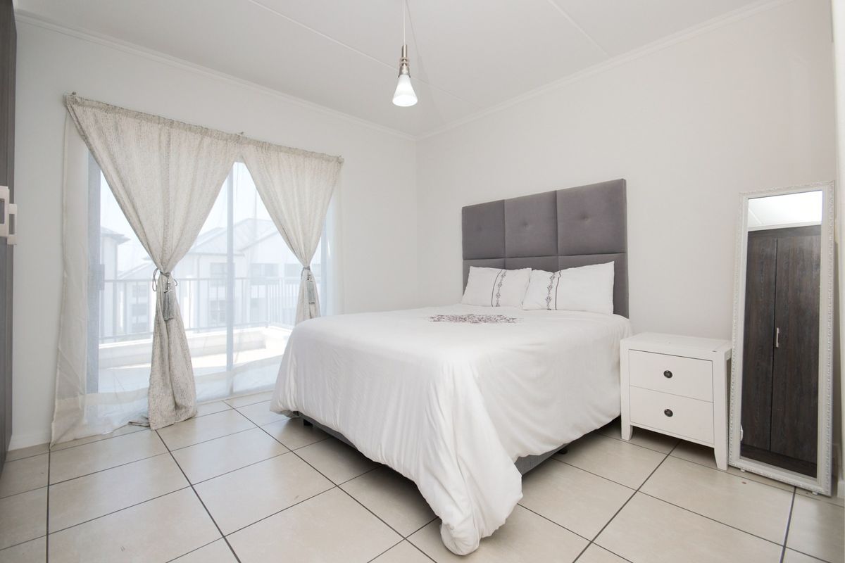A bright bedroom featuring neutral tiled flooring, a coved ceiling, and a sliding glass door providing access to an outdoor balcony area.