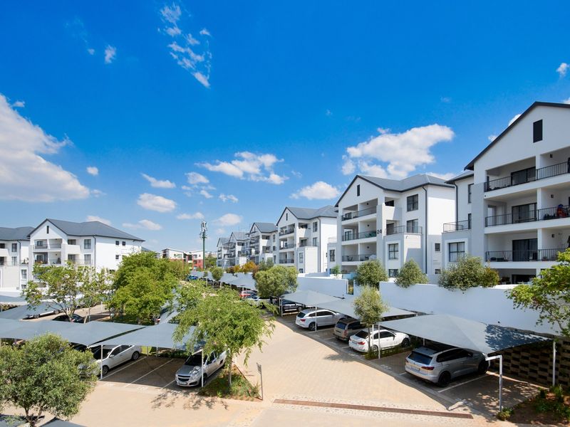 An elevated view of a modern apartment complex featuring multiple residential buildings, paved driveways, and covered parking bays.