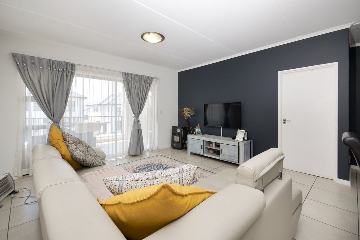 A bright living room featuring tiled flooring, a dark accent wall, and a sliding glass door providing access to an outdoor balcony area.