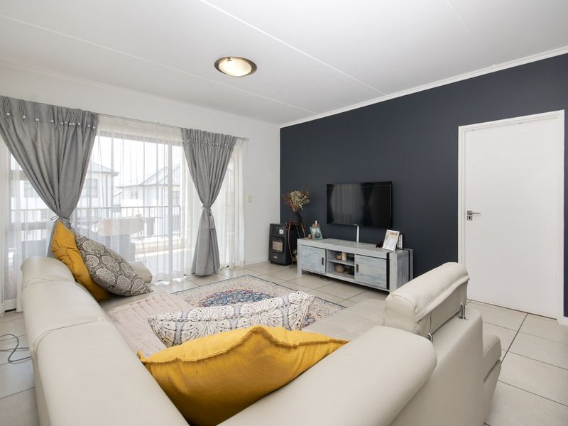 A bright living room featuring tiled flooring, a dark accent wall, and a sliding glass door providing access to an outdoor balcony area.