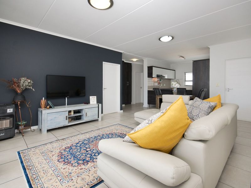 An open-plan living and kitchen area featuring tiled flooring, modern dark accent wall, and functional kitchen cabinetry with integrated appliances.
