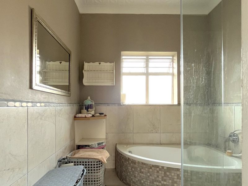 A bathroom featuring a corner bathtub with mosaic tiling, a glass shower enclosure, and neutral wall tiles.