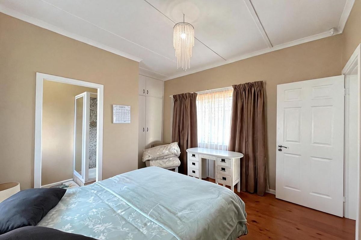 A bedroom featuring timber flooring, built-in cupboards, and an en-suite bathroom access, offering a functional layout with neutral wall tones.