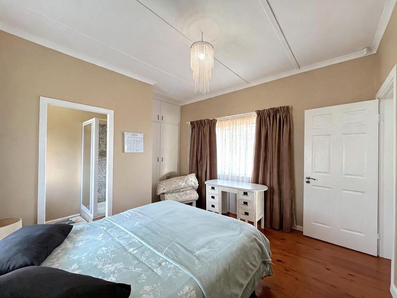 A bedroom featuring timber flooring, built-in cupboards, and an en-suite bathroom access, offering a functional layout with neutral wall tones.