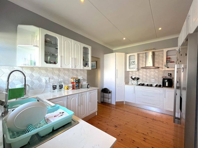 A well-maintained kitchen featuring white cabinetry, stone countertops, a gas hob with extractor fan, and warm timber flooring.