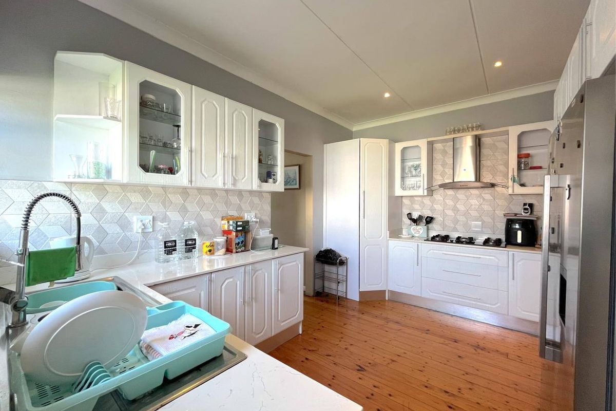 A well-maintained kitchen featuring white cabinetry, stone countertops, a gas hob with extractor fan, and warm timber flooring.