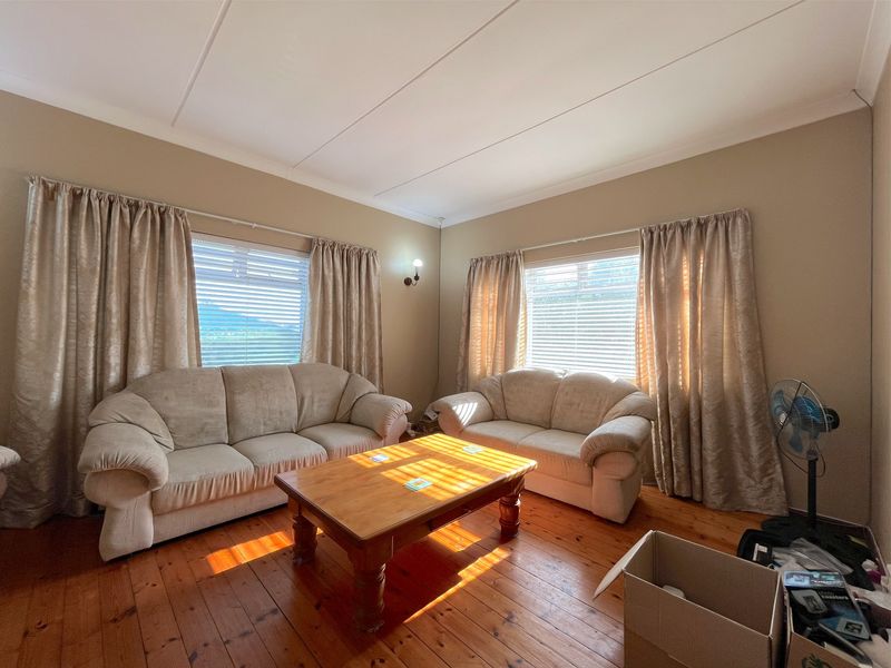 A living room featuring polished timber flooring, coved ceilings, and dual windows with natural light.
