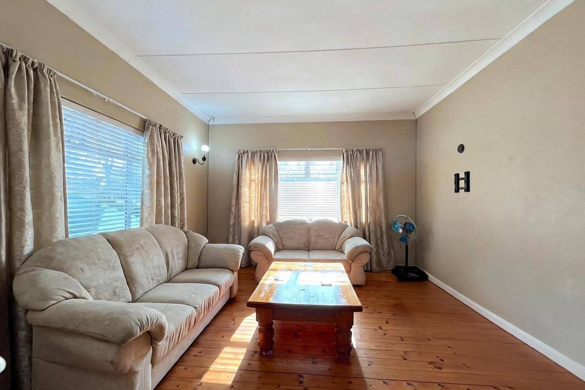 A living room featuring warm timber flooring, neutral wall tones, and natural light through dual window sets with fitted blinds.