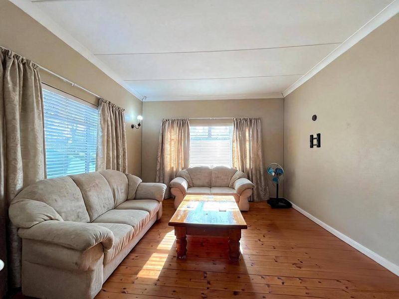 A living room featuring warm timber flooring, neutral wall tones, and natural light through dual window sets with fitted blinds.