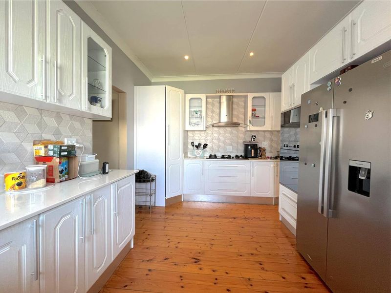 A well-maintained kitchen featuring white cabinetry, a gas hob with extractor fan, built-in oven, tiled backsplash, and warm timber flooring.
